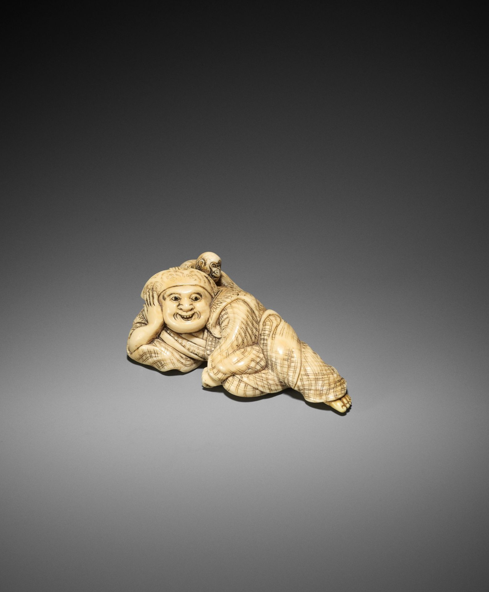 YOSHINAGA: A LARGE AND EXCEPTIONAL IVORY NETSUKE OF A RECLINING SARUMAWASHI WITH MONKEY