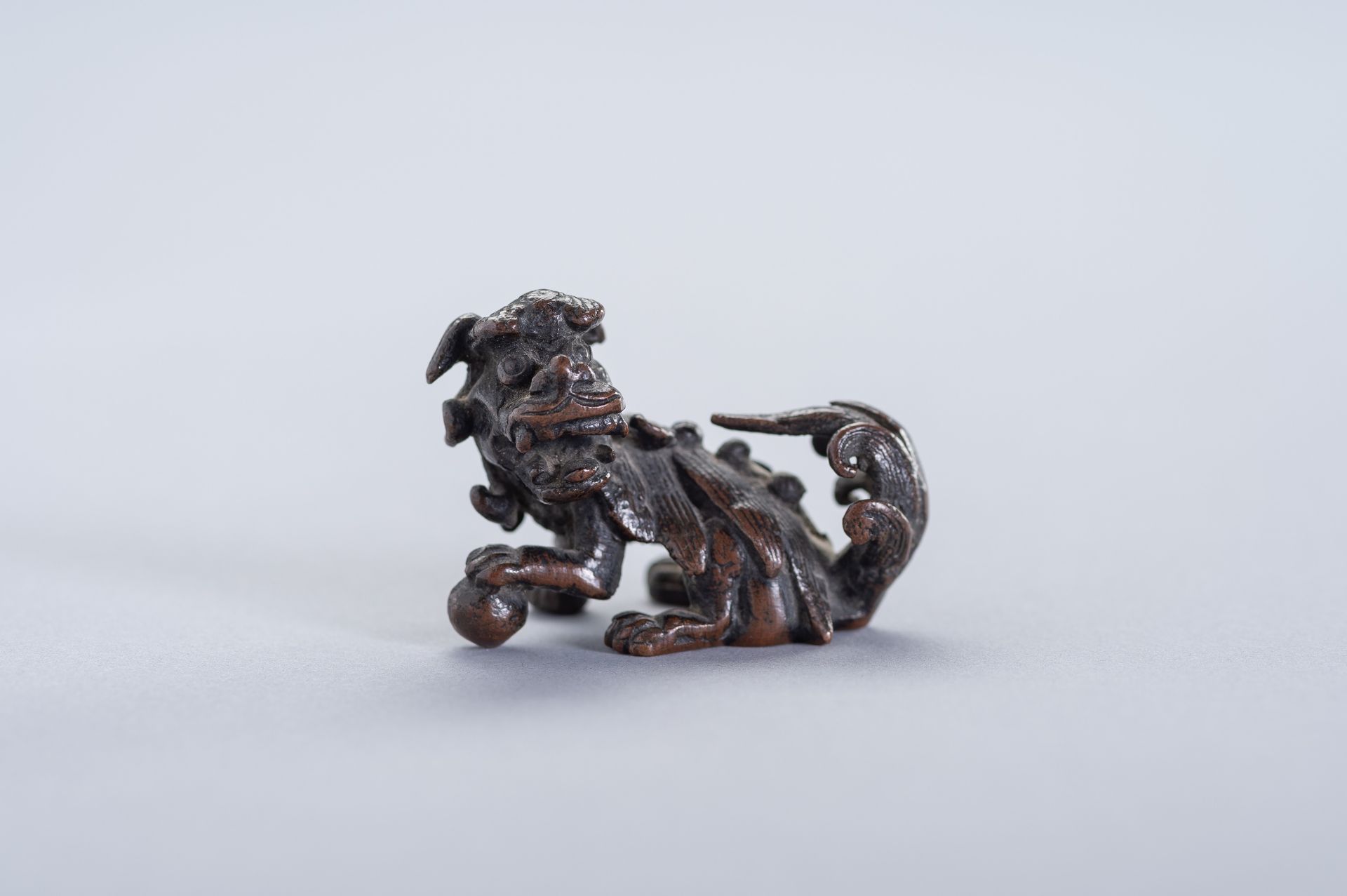 A MINIATURE BRONZE FIGURE OF A BUDDHIST LION