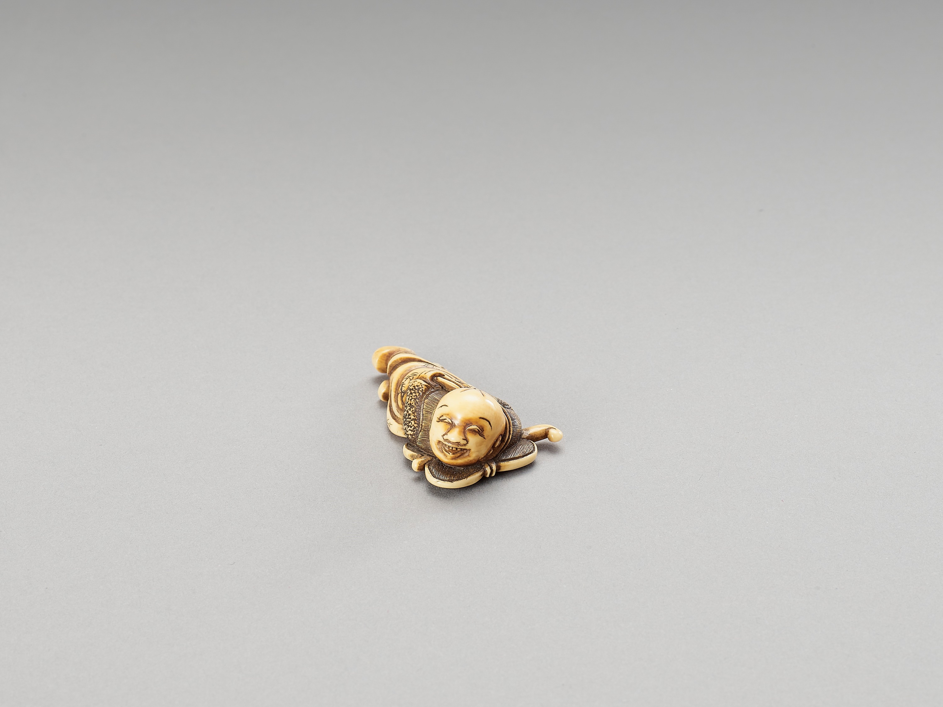 A HIDEMASA-SCHOOL IVORY NETSUKE OF A KARAKO ON A FAN