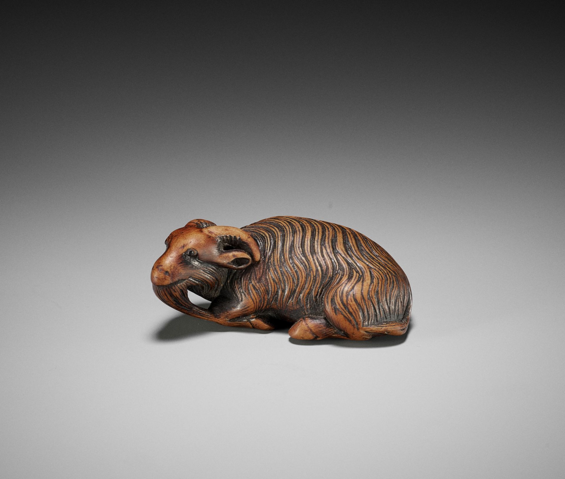 A FINE KYOTO SCHOOL WOOD NETSUKE OF A RECUMBENT GOAT