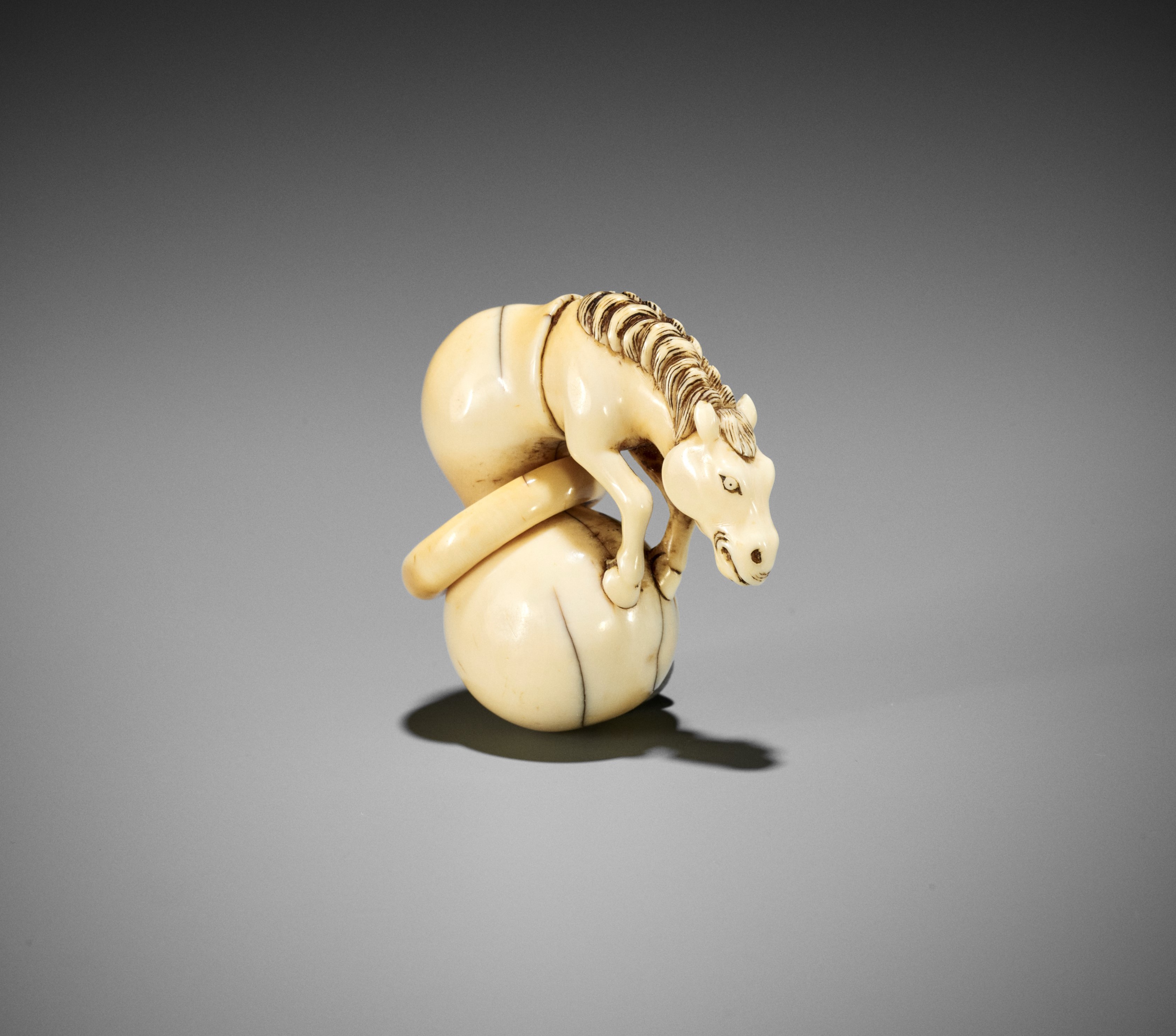 A GOOD IVORY NETSUKE OF CHOKARO'S HORSE EMERGING FROM A DOUBLE GOURD