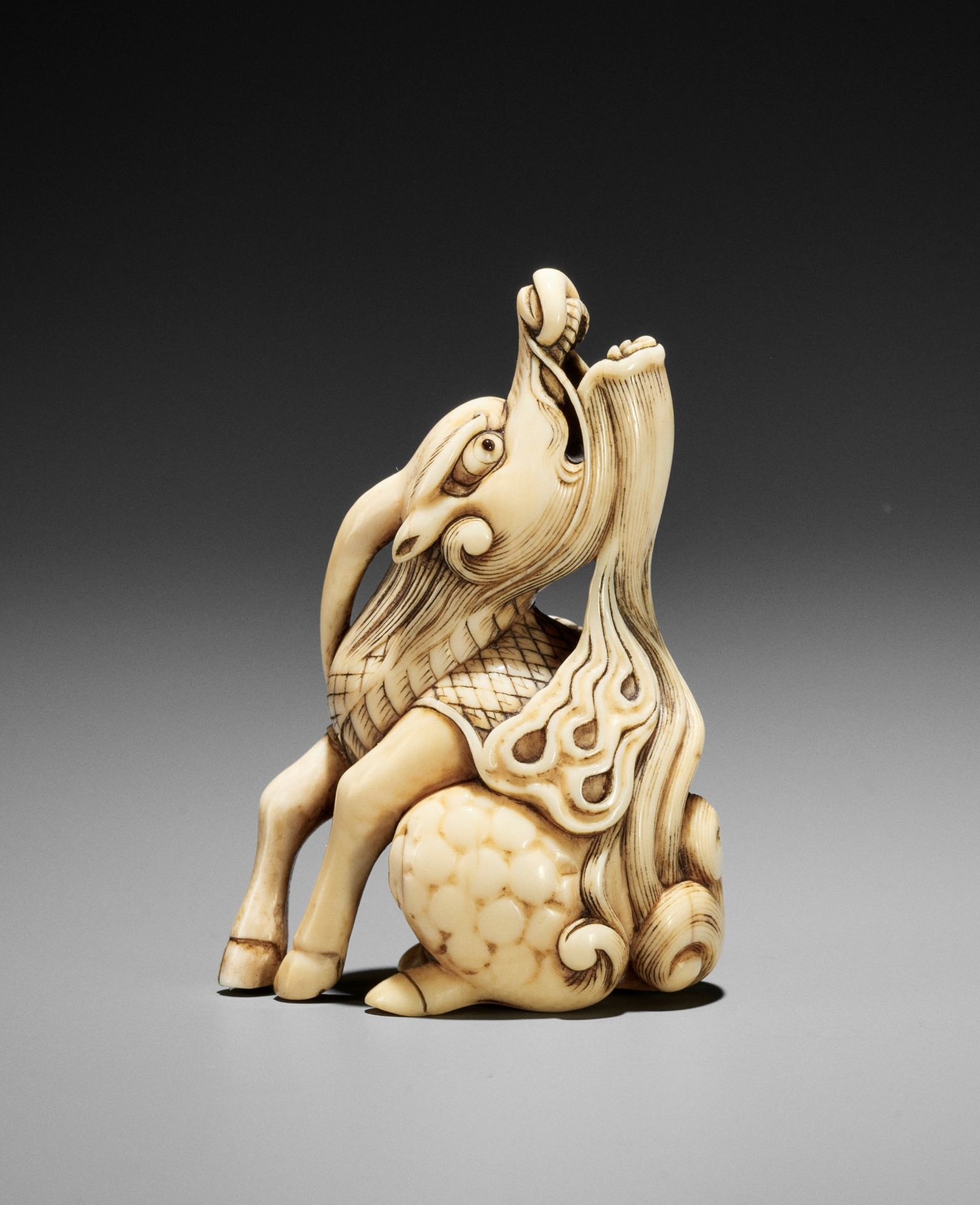 A POWERFUL IVORY NETSUKE OF A BAYING KIRIN, ATTRIBUTED TO MITSUHARU