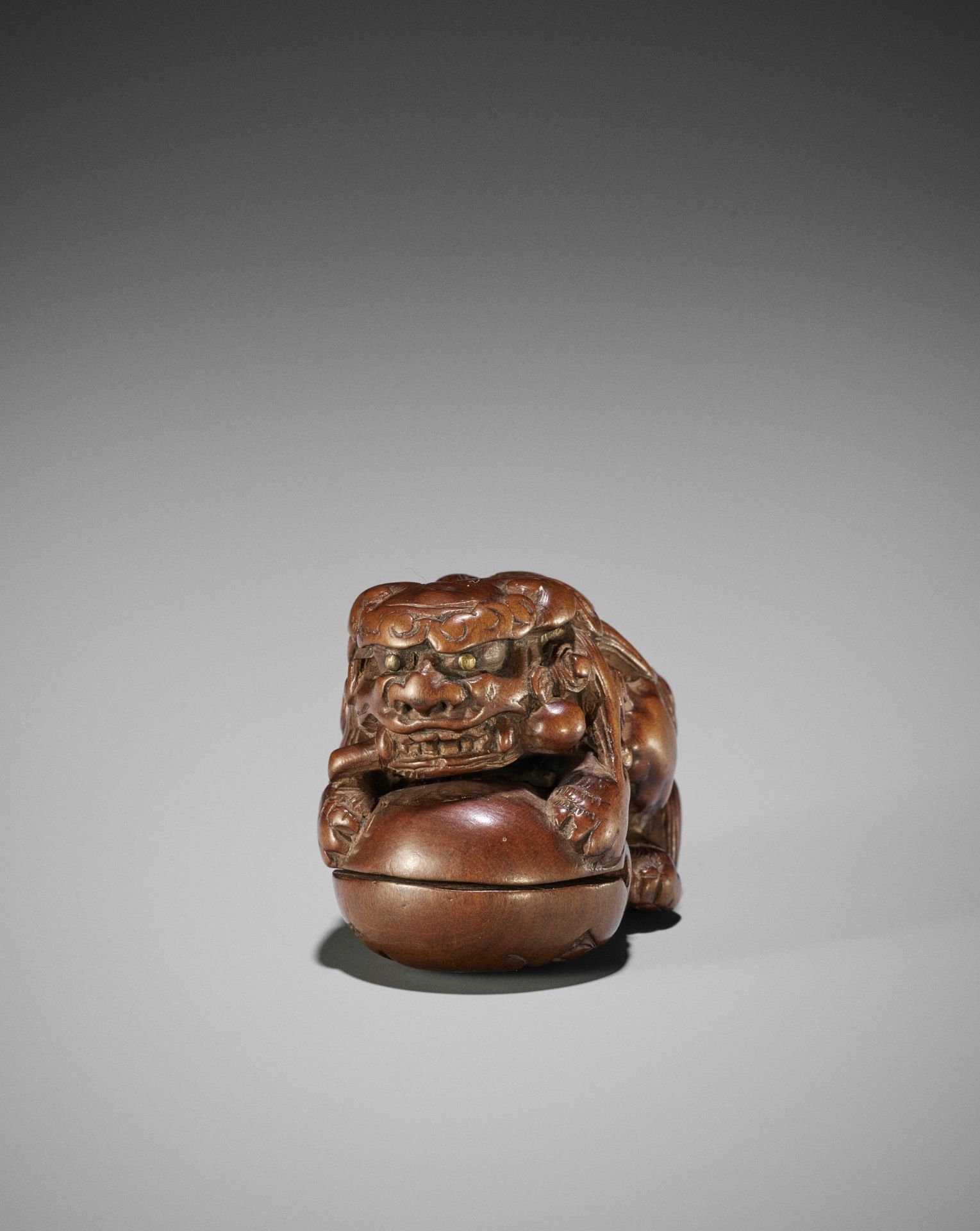 AN EARLY WOOD NETSUKE OF A SHISHI ON A MOKUGYO