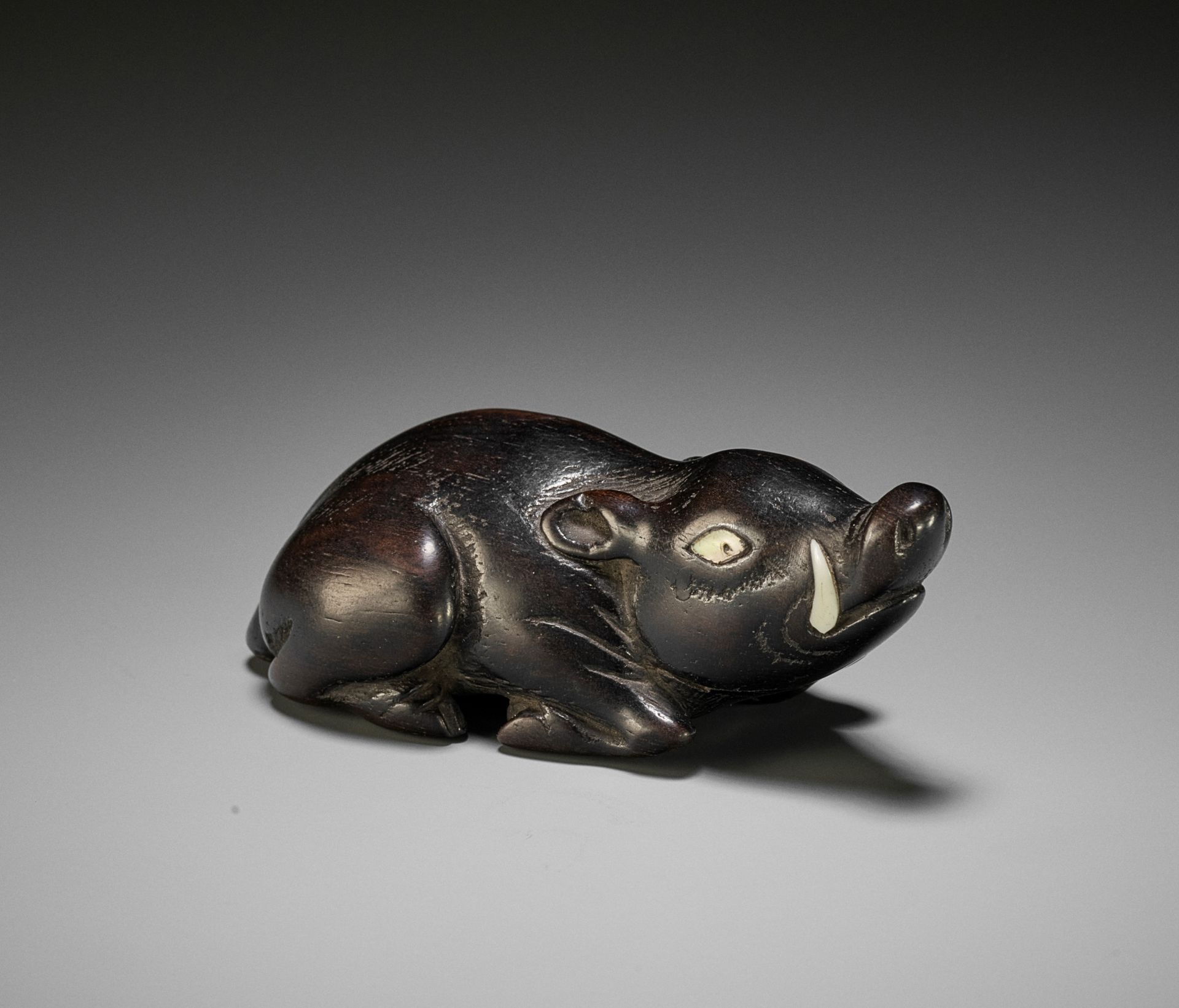 A LARGE AND OLD DARK WOOD NETSUKE OF A RECUMBENT BOAR