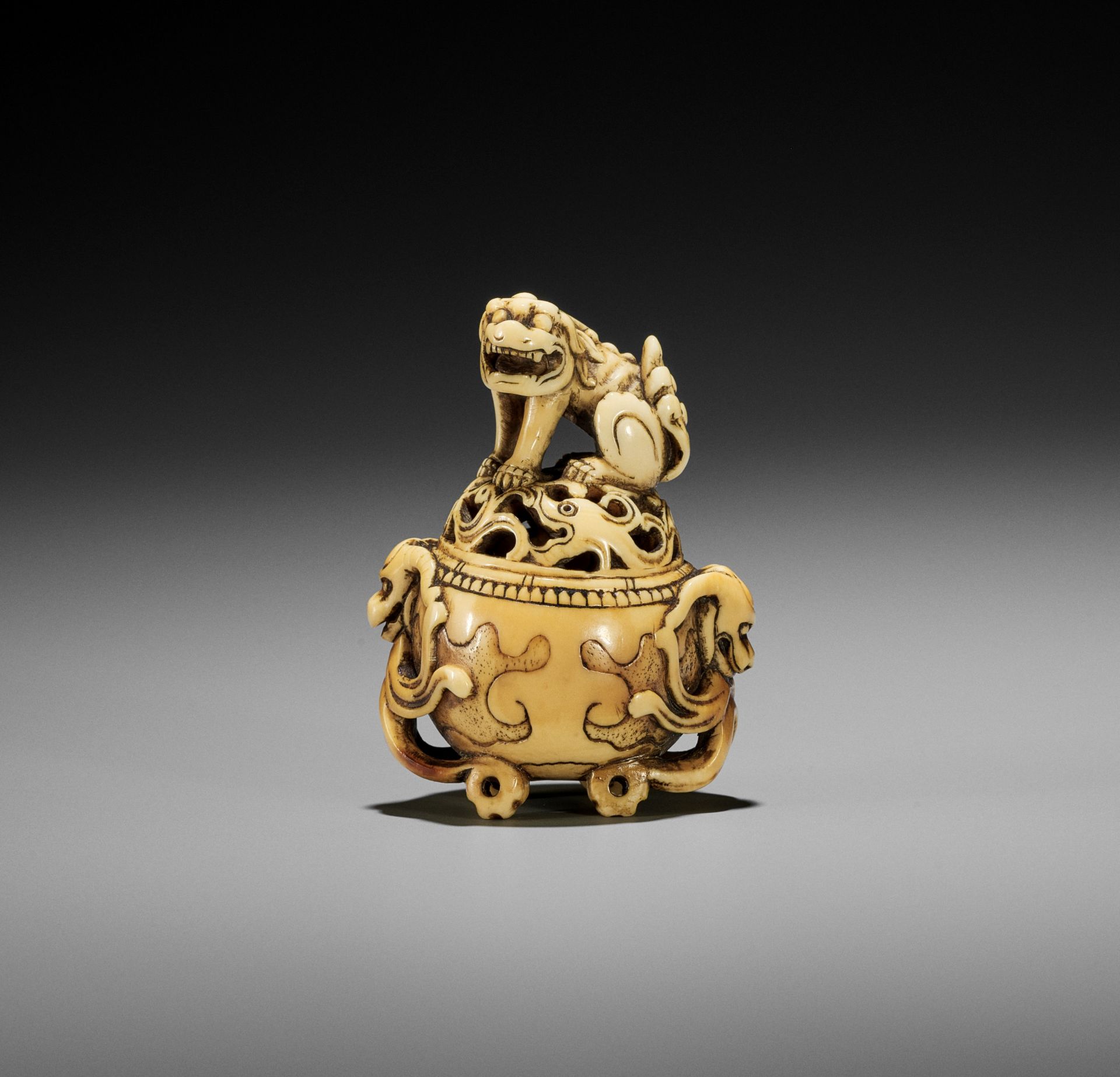 A RARE IVORY NETSUKE OF A KORO (INCENSE BURNER) WITH SHISHI