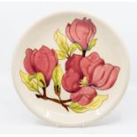 A Moorcroft Magnolia pattern plate, tube lined decoration on a cream ground, 26cm in diameter,