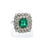 An emerald and diamond 18ct white gold cluster ring, comprising an emerald cut emerald set to the