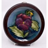Moorcroft: A Walter Moorcroft 'Pansy' pattern coaster on a blue/green ground in a wooden frame.