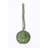 A Chinese green jade circular pendant, carved and having a pierced centre, having a brass chain