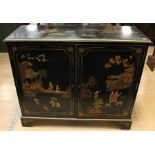 A Japanese style black lacquered side cabinet, fitted with two doors depicting figures in a garden