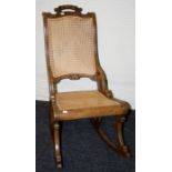 An ealy 20th century cane upholstered rocking chair with florally carved handle to rail