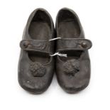 A pair of 19th Century pewter children's shoes with button strap and ball decoration