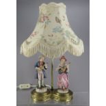 A brass-based table lamp and shade with two Continental porcelain figures of a boy and a girl.  In