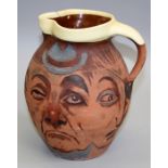 A 19th century terracotta loop handled jug, painted in the round with faces of early 20th century
