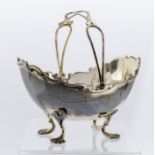 A George V silver sugar bowl, helmet shaped with wavy rim, on four scroll and trefid feet, swing