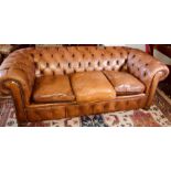 A Victorian revival tan leather three seater Chesterfield sofa, scrolling button back and arms,