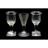 A pair of early nineteenth century pedestal wine glasses on square feet with flared openings and