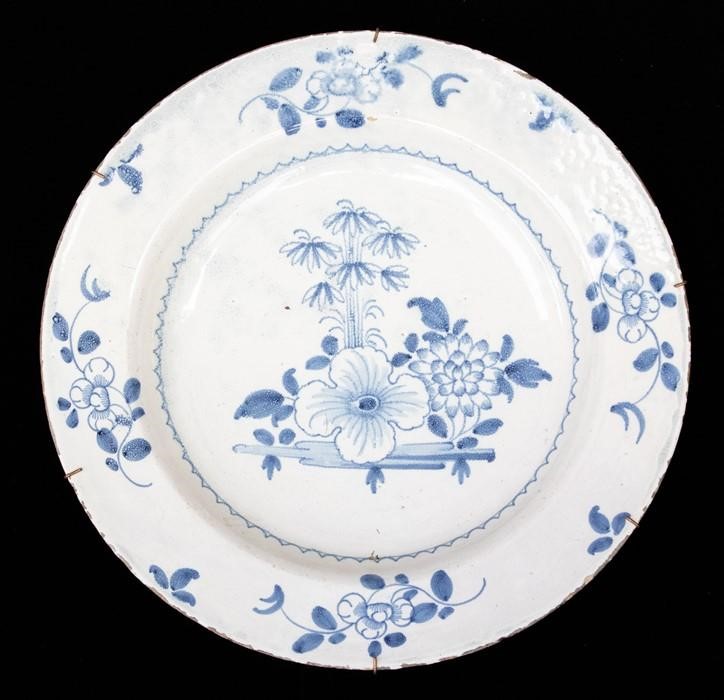 An English Delft polychrome blue and white charger decorated with central floral decoration, the