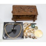 A carved wooden box containing costume jewellery including faux pearl necklaces, gilt metal