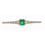 An emerald and diamond bar brooch, rub over set to the centre with a rectangular cut emerald,