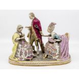 A German porcelain figurative group with two seated women and a Gentleman standing beside a plinth