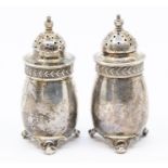 A matched pair of George V silver pepperettes with decorated borders on scroll feet, with domed