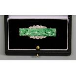 An Art Deco jade and diamond set brooch, comprising a rectangular carved jade with a scalloped