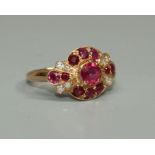 A ruby and diamond set unmarked rose gold ring, the round central claw set ruby within a surround of