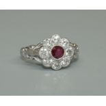 A ruby and diamond flower platinum cluster ring, comprising a central round cut ruby, rub over