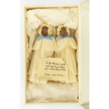 A pair of chocolate dolls, 1923, in crepe paper gowns and bonnets, with blue silk bows; together