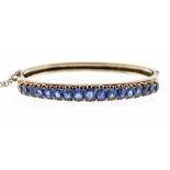 A sapphire and 14ct gold hinged bangle, set with a row of seventeen graduated oval claw set