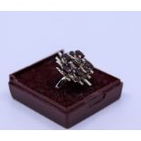 An 18k white gold garnet cluster ring, claw set, seven oval and garnet, stamped 18k, approx 5g