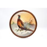 A circular porcelain plaque probably Minton painted with a Pheasant in wintry landscape, signed J