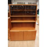 A 1970s teak cabinet, fitted with a glazed section to top with a shelf below, fitted with solid