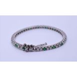 A white metal diamond and emerald bracelet, grain set thirty-four round brilliant-cut emeralds,