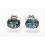 A pair of silver and blue topaz stud earrings, claw set with oval blue topaz,  approx. 7 x 5mm, post