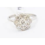 A diamond and platinum flower cluster set ring, comprising a central rub over set brilliant cut