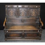 An early 20th century oak settle, the egg and dart rail over heraldic three panel back, downswept