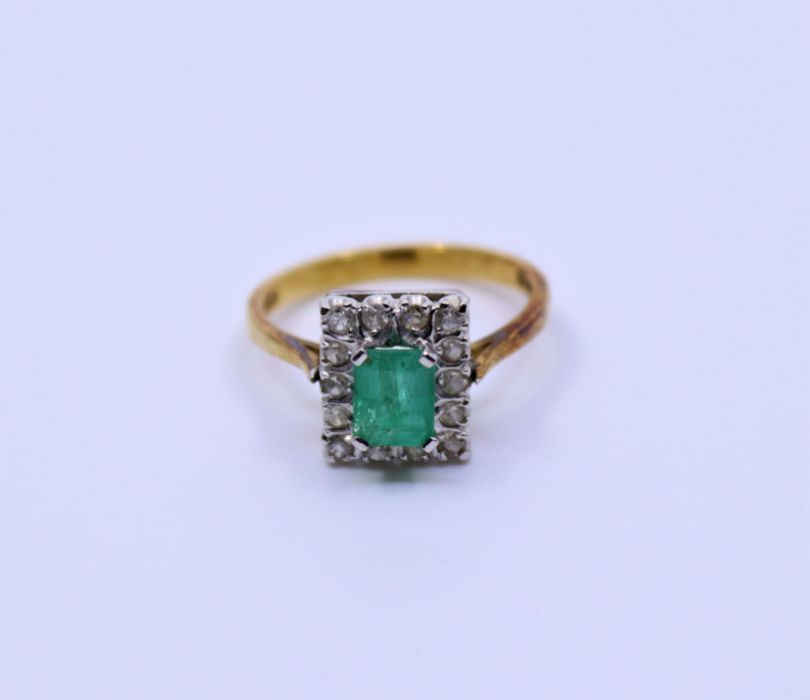 An 18ct emerald and diamond cluster ring, claw set emerald-cut emerald and fourteen eight-cut