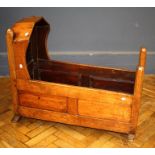 A 19th century pitched pine rocking cradle, of pegged and panel construction, on sledge end