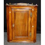An 18th century oak wall mounting corner cupboard, the panel door with brass furniture, enclosing