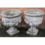 A pair of reconstituted stone garden pedestal urns, each with moulded ribbon tied swag decoration on