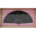 A Spanish black lace and sequin decorated fan, with carved ebonized sticks in a wall mounting