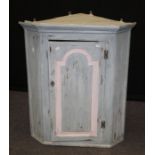 An early 19th century later painted wall mounting corner cupboard, the arched panel door enclosing