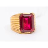 A synthetic ruby and rose metal dress ring, comprising a rub over set emerald cut synthetic ruby,