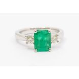 An emerald and diamond 18ct white gold ring, comprising a claw set emerald to the centre, emerald