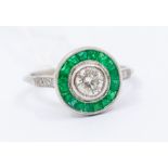 A diamond and emerald platinum set ring, the central rub-over set round brilliant cut diamond