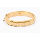 A 9ct gold hinged bangle, hollow form with engraved foliate decoration, width approx. 12mm, inner