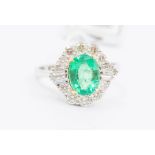 An emerald and diamond 18ct white gold cluster ring, comprising a central oval cut emerald,  approx.