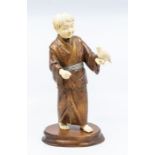 An early 20th century Meiji/Taisho period ivory and hardwood okimono, he stands with a bird